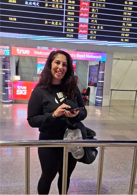 Woman smiling at an airport holding her phone.