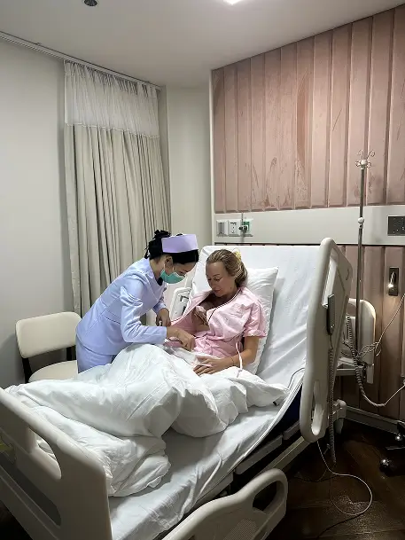 Julia receiving attentive care from a nurse while resting in her private hospital bed in Bangkok