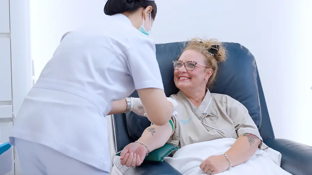 Nurse checks a smiling patient’s blood pressure in a clinic chair.