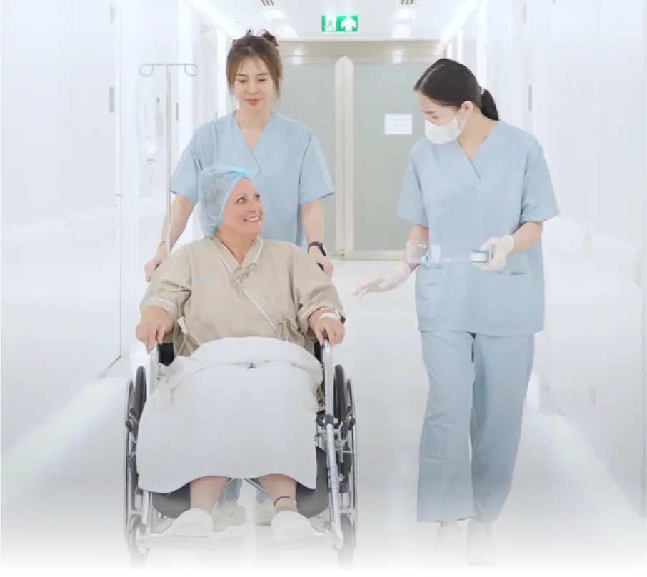 Medical staff assist a patient in a wheelchair along a hospital corridor.