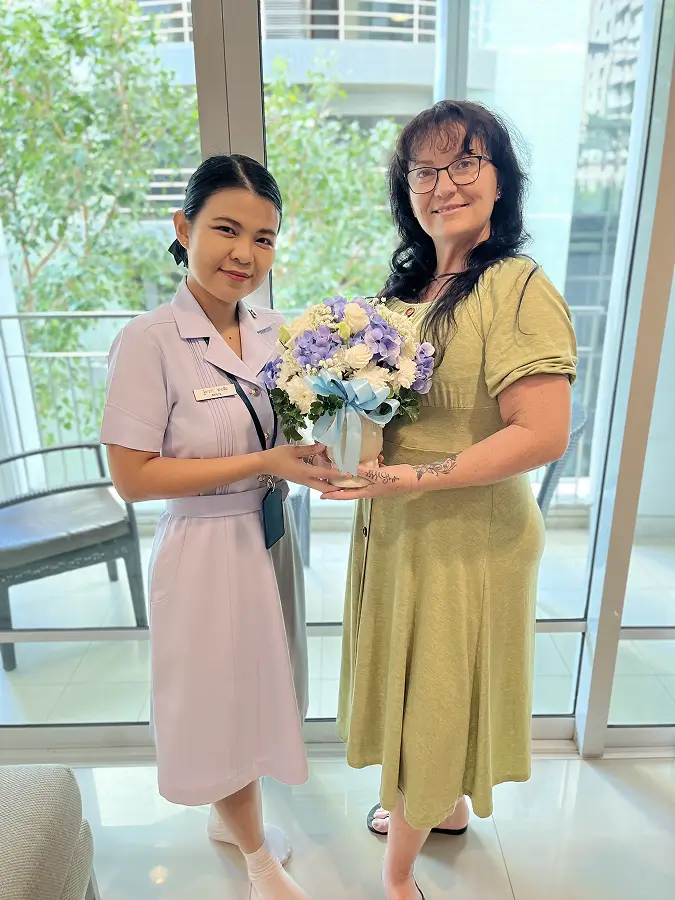 Janessa and Nurse Fah holding a flower arrangement during a recovery visit.