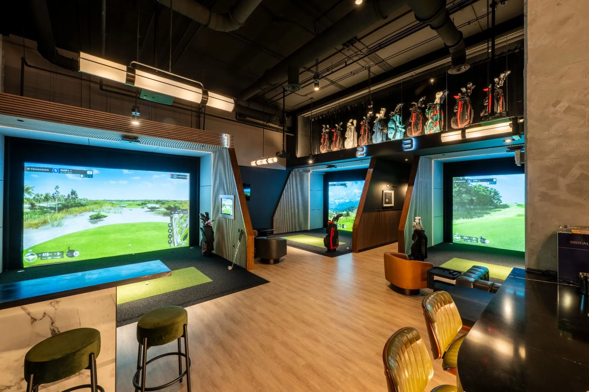 Interior view of two indoor golf simulator bays with modern lighting, marble high-top table, and green bar stools. The Tips Golf Miami Brickell.