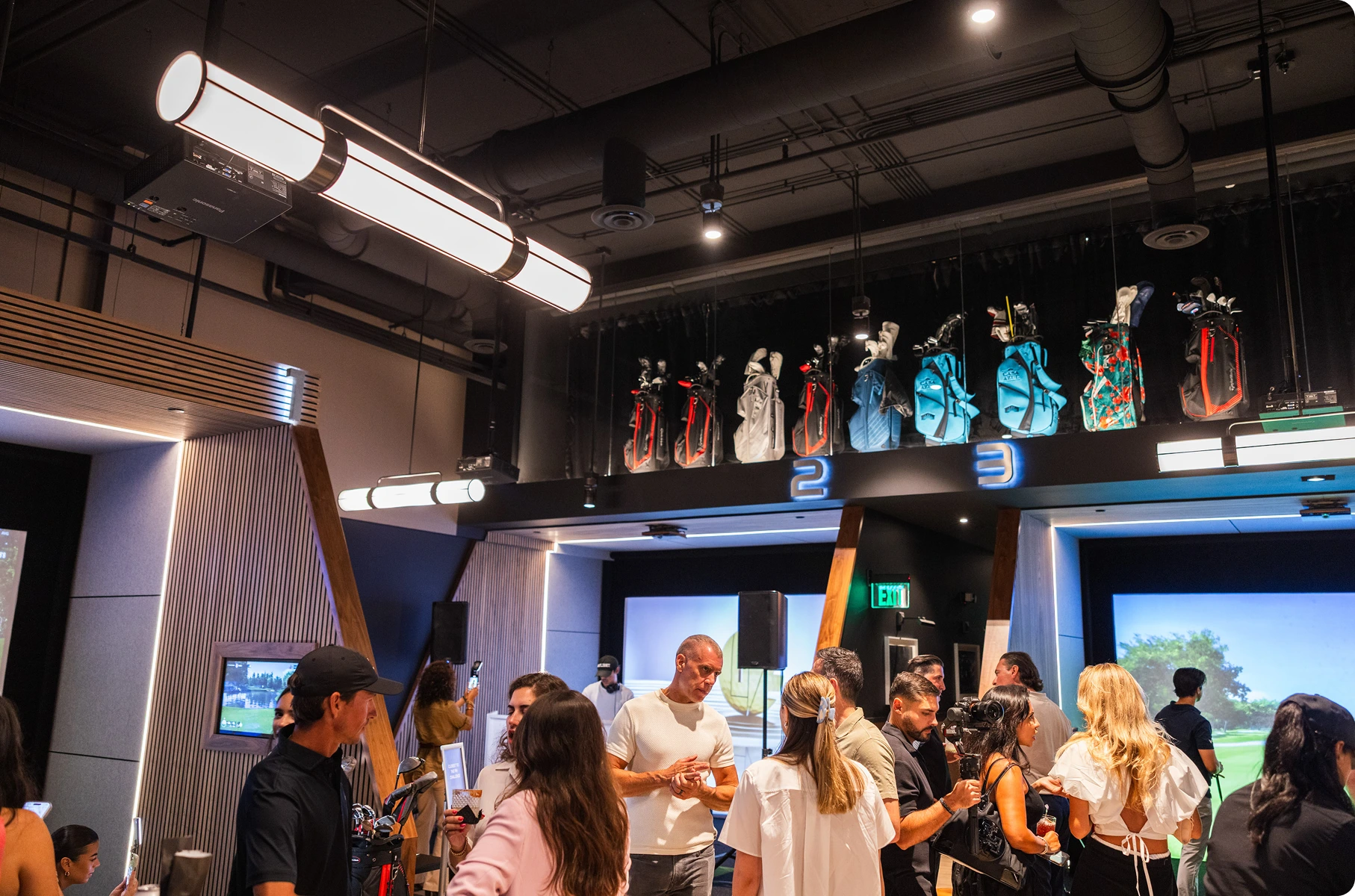 Crowd gathered around the simulator bays at a private event, guests mingling and talking.