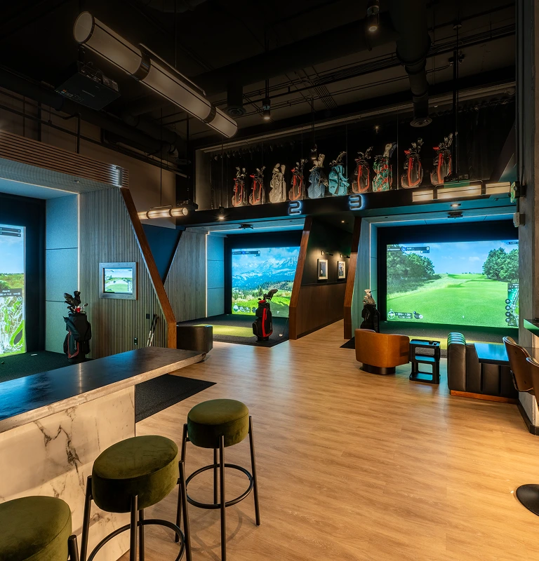 Modern lounge with three golf simulator bays, marble high-top, and green velvet bar stools.