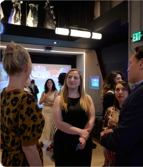 A group of adults engaged in conversation at an indoor social event with modern lighting and decor.