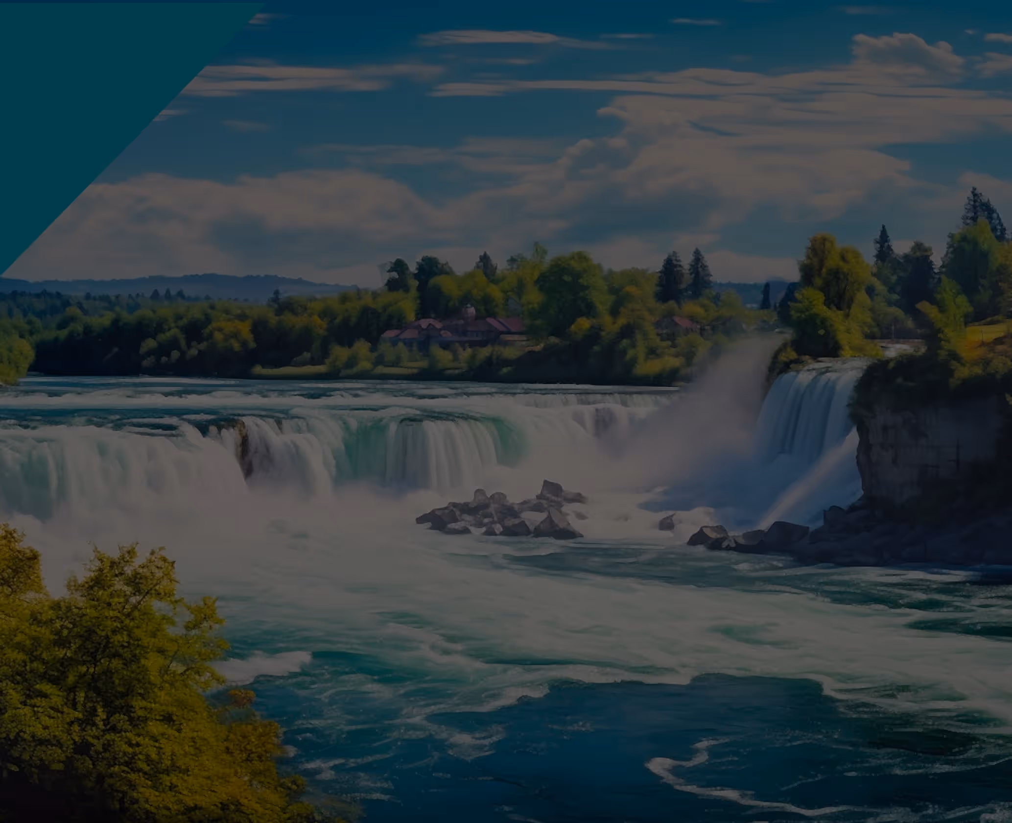 Wide view of a large waterfall surrounded by lush green trees and a partly cloudy sky.