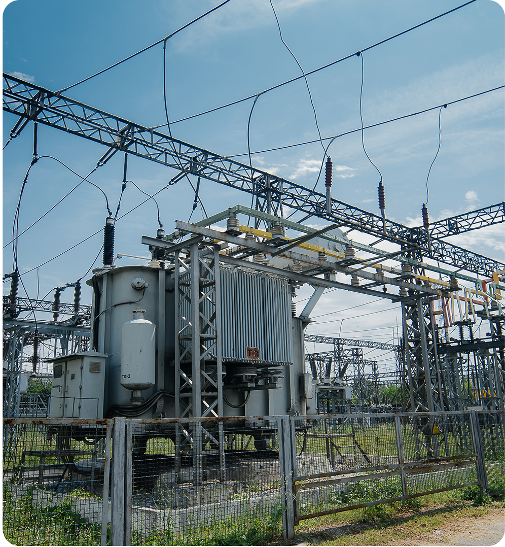 Electrical transformer and power lines at an outdoor electrical substation under a blue sky.