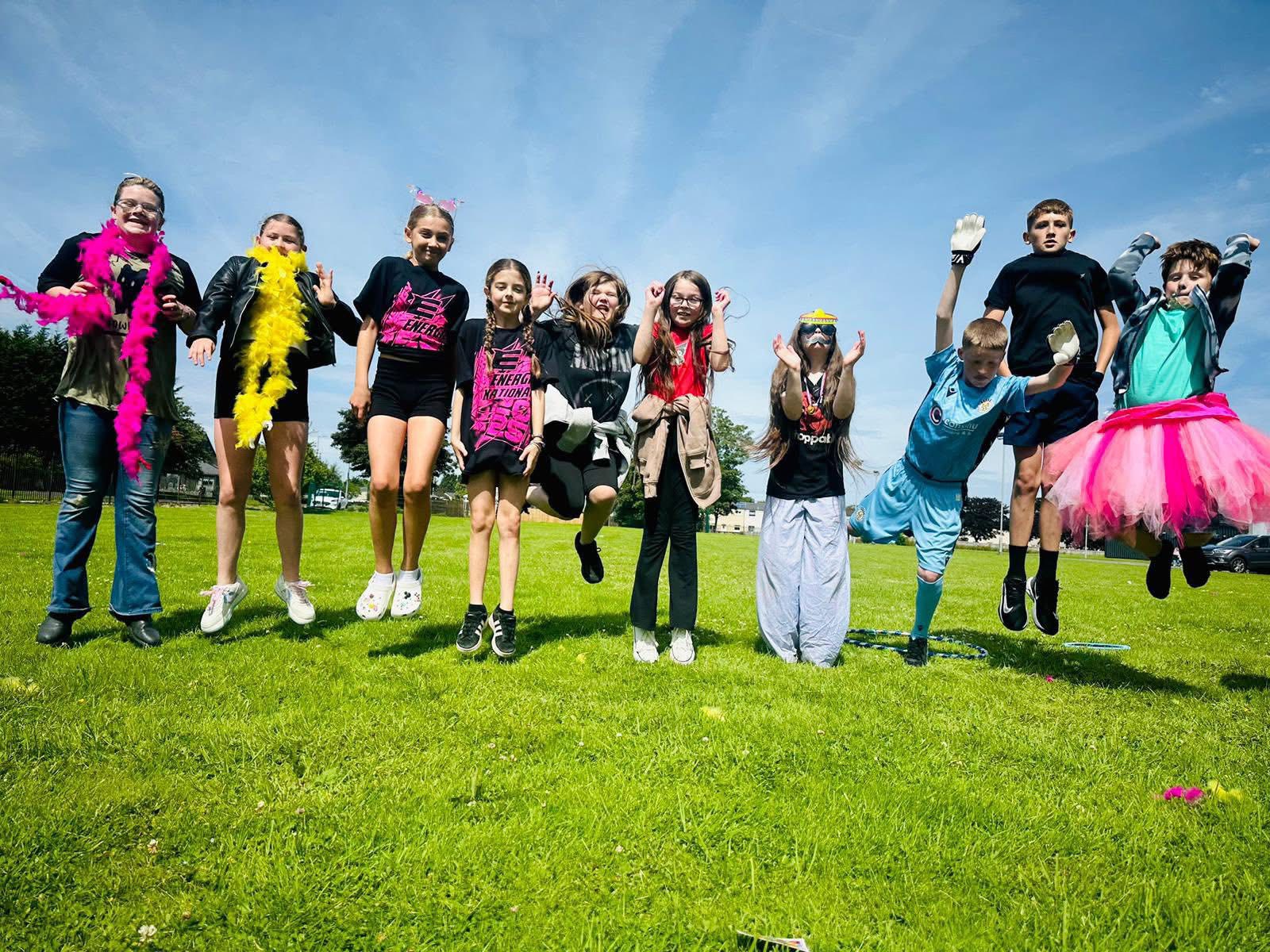 A group of young people mid-jump on a grass field on a sunny day