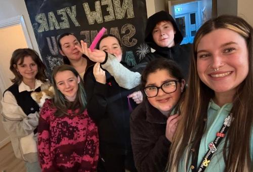 A group of young people and a youth worker taking a selfie indoors in front of a New Year chalkboard sign