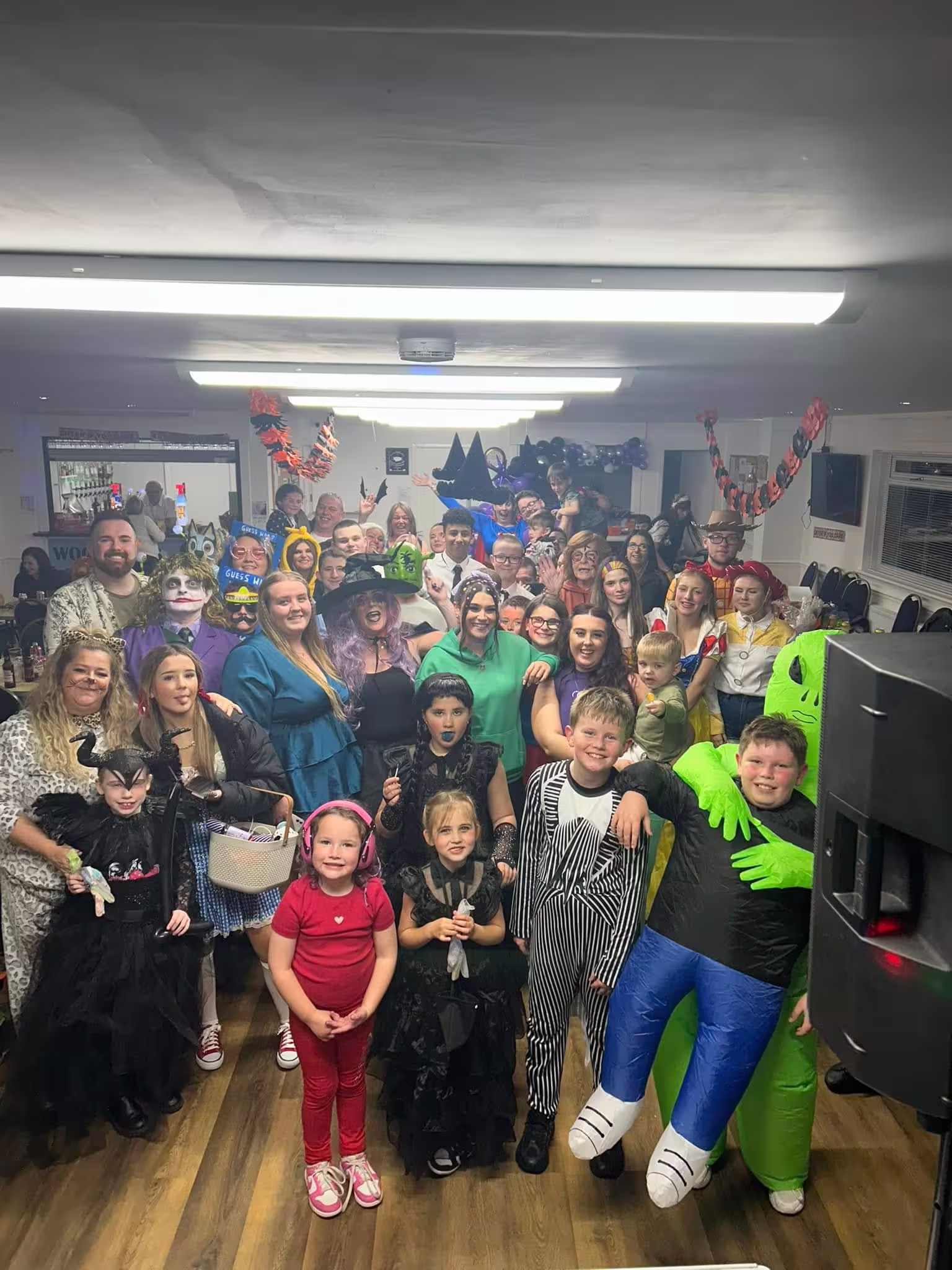 A large group of adults and young people in fancy dress at a halloween event, posing together and smiling at the camera.