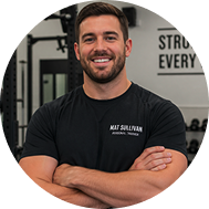 Smiling man with folded arms in gym wearing a black shirt labeled 'Matt Sullivan Personal Trainer.'