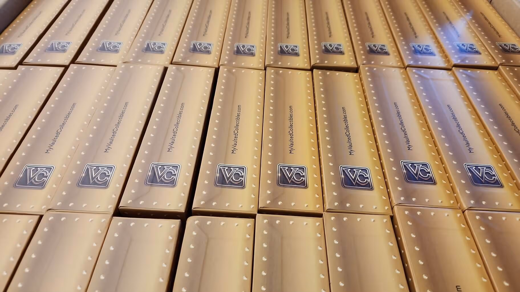 Rows of closed beige and gold collector boxes with VC logos and MyVaultedCollectibles.com text.