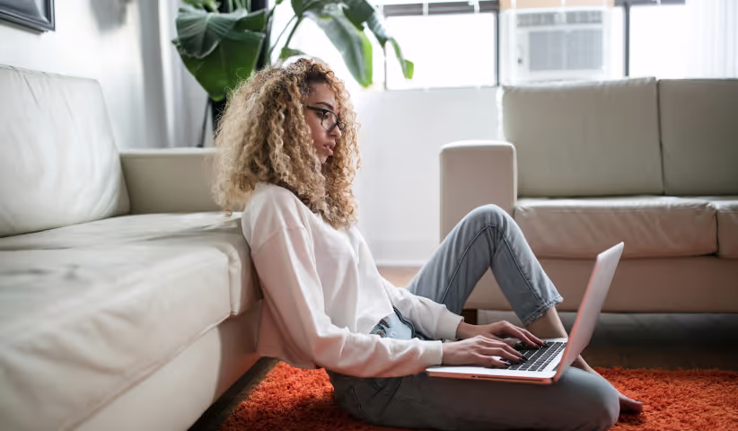 Eine Frau sitzt auf dem Boden und arbeitet an ihrem Laptop.