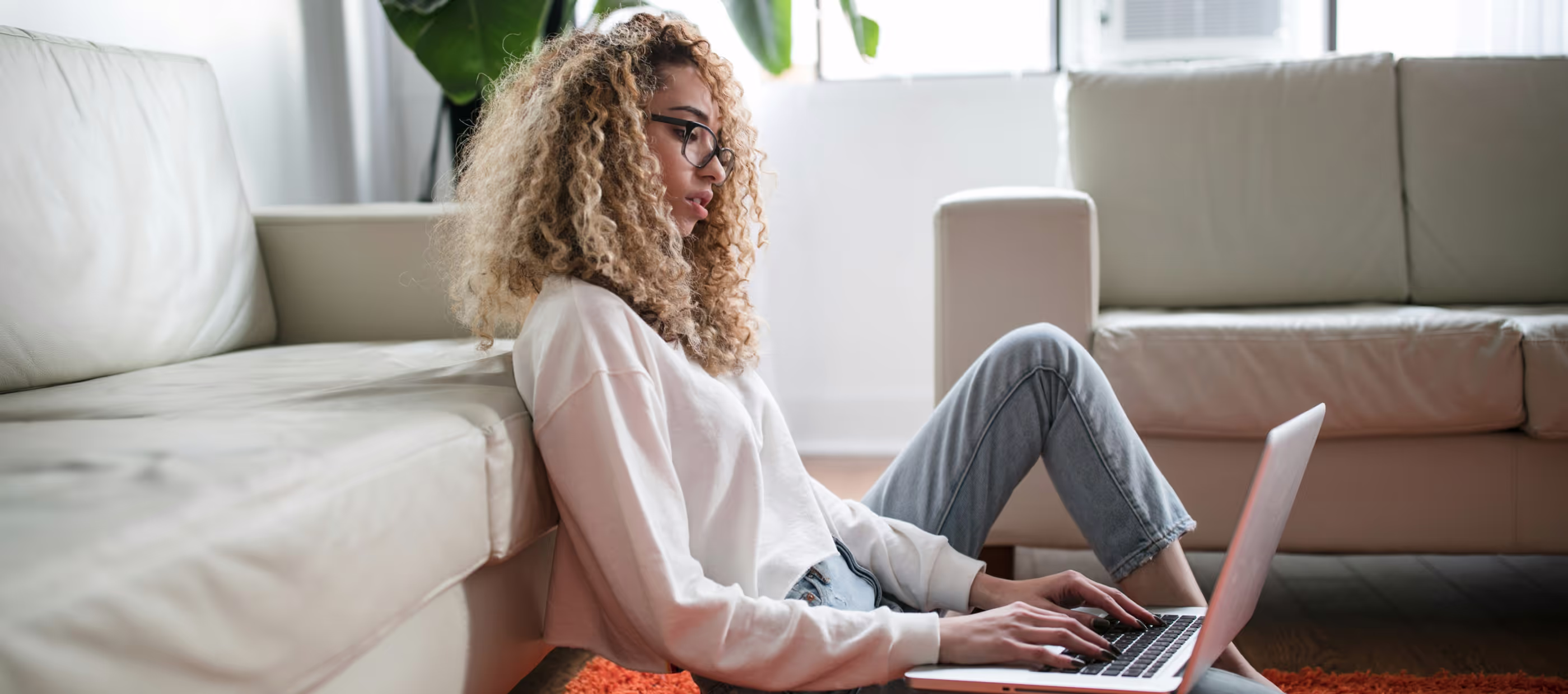 Une femme assise au sol travaille sur son ordinateur portable.