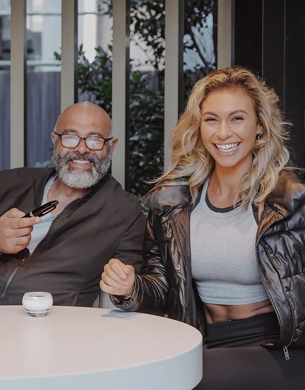 A man and a woman laughing together sitting at a table, one is holding a pen and they are enjoying a relaxed, happy moment.