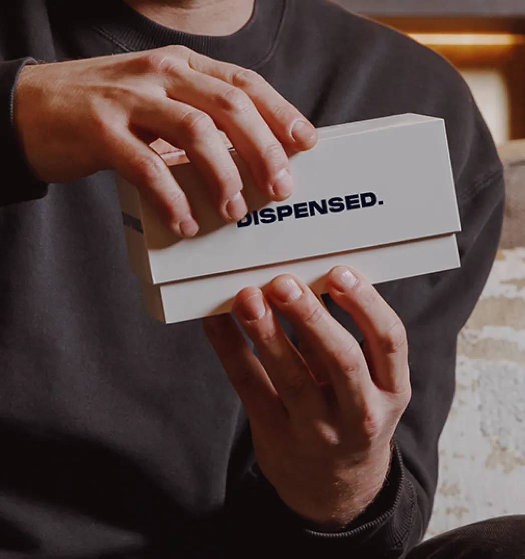 Close-up of a man as he opens a Dispensed medical delivery box in a warmly lit living room.