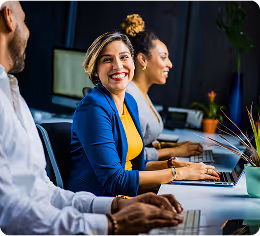 Three diverse colleagues working at computers in an office, one woman smiling at the camera.