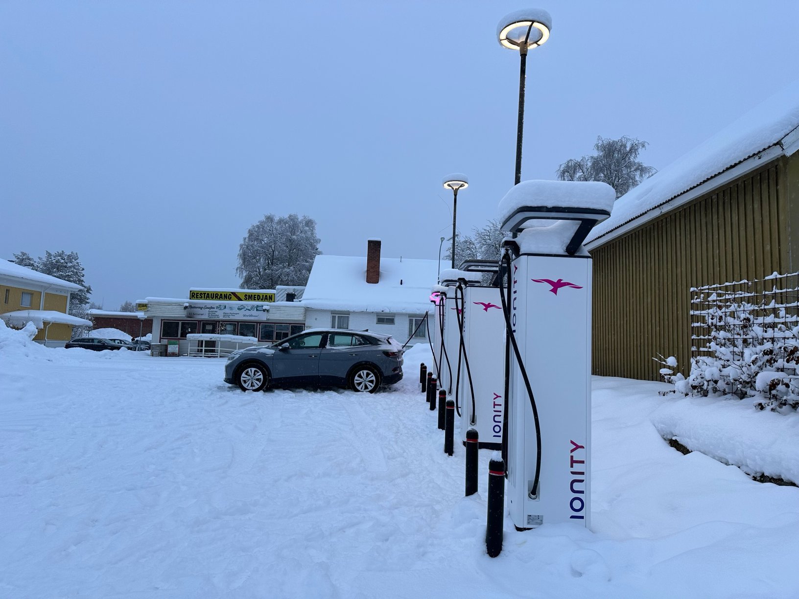 Bluish-grey electric car charging at an IONITY station in a snowy landscape