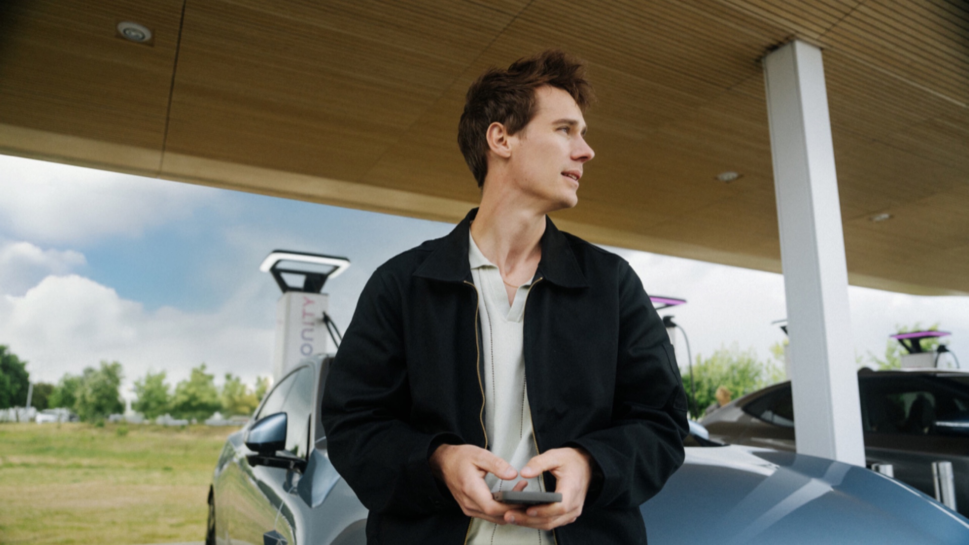Man leans against a car while fast charging at an IONITY Location