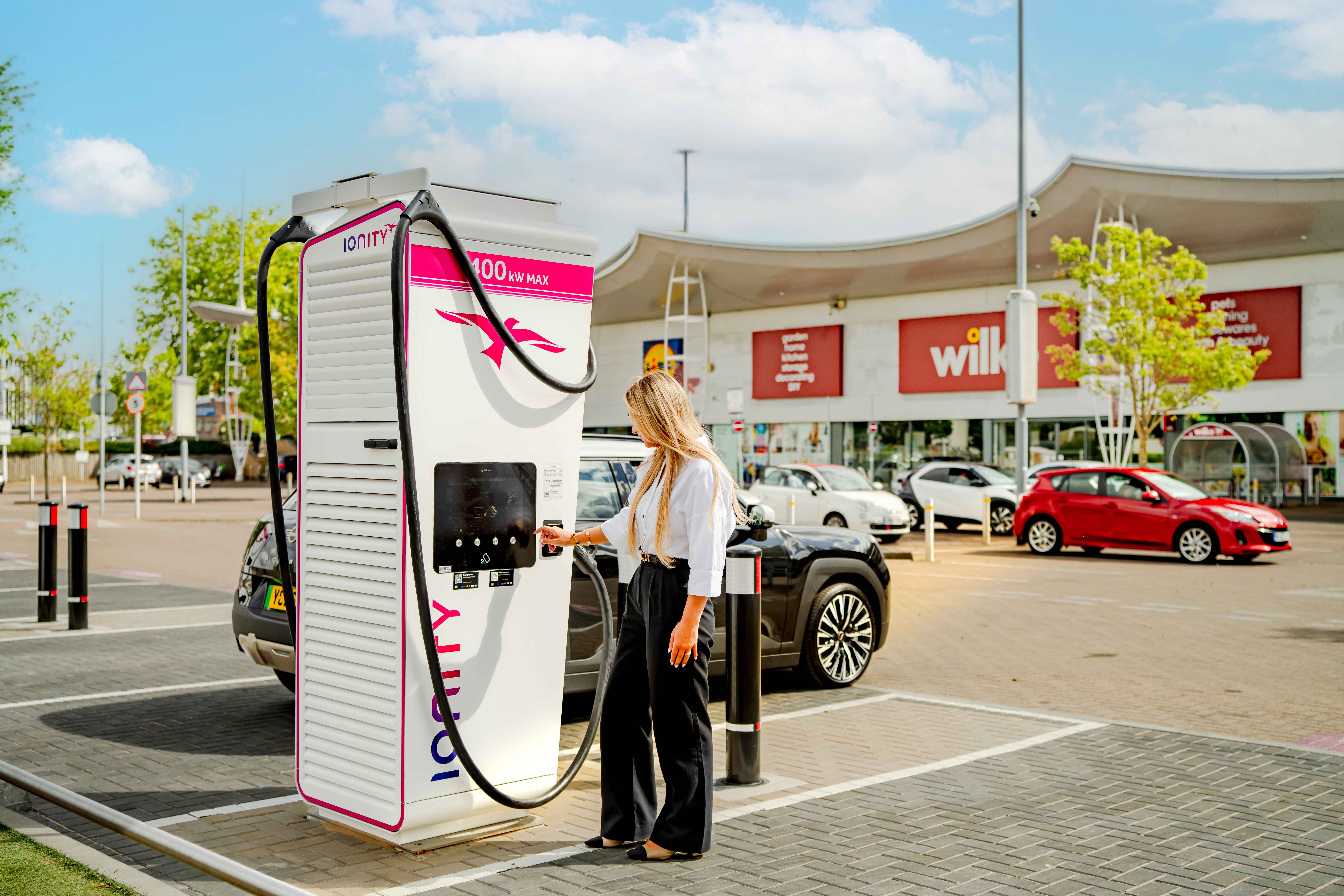 A woman uses an ultra-fast charger to charge a black electric car at the new IONITY Greenwich charging site