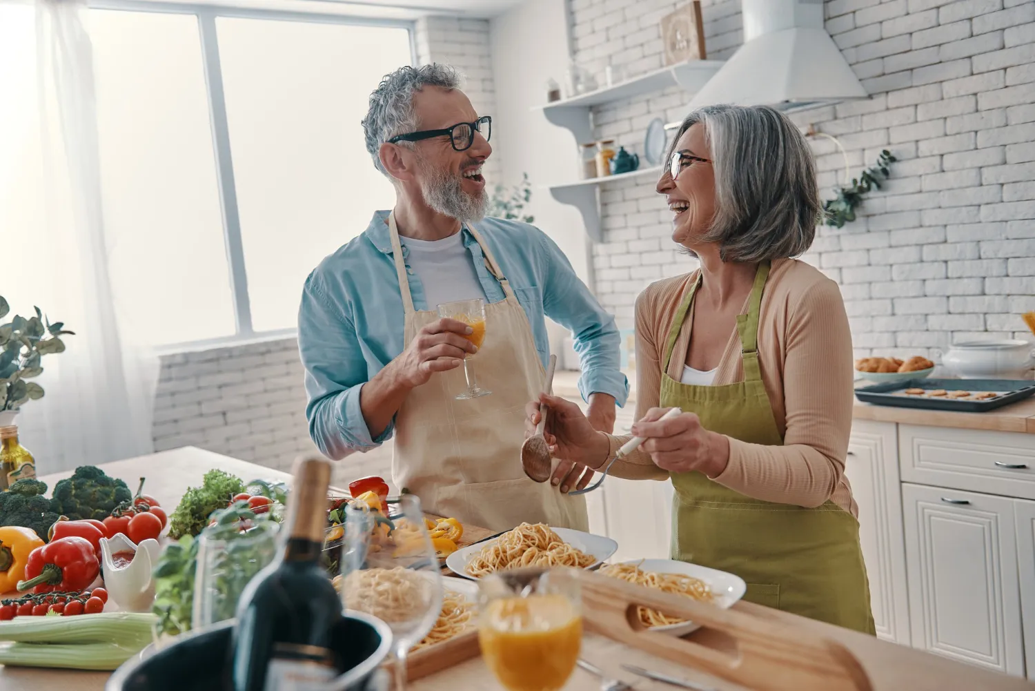Modern senior couple in aprons preparing healthy dinner and smiling.