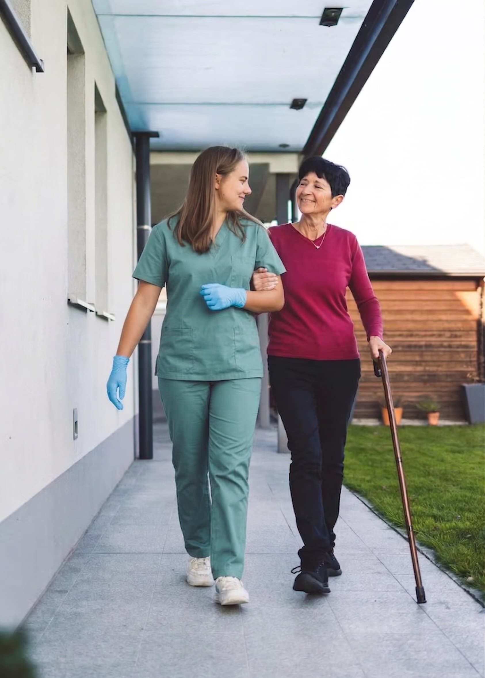 Noah's Dove caregiver assisting an elderly woman walking with a cane outdoors for daily exercise.
