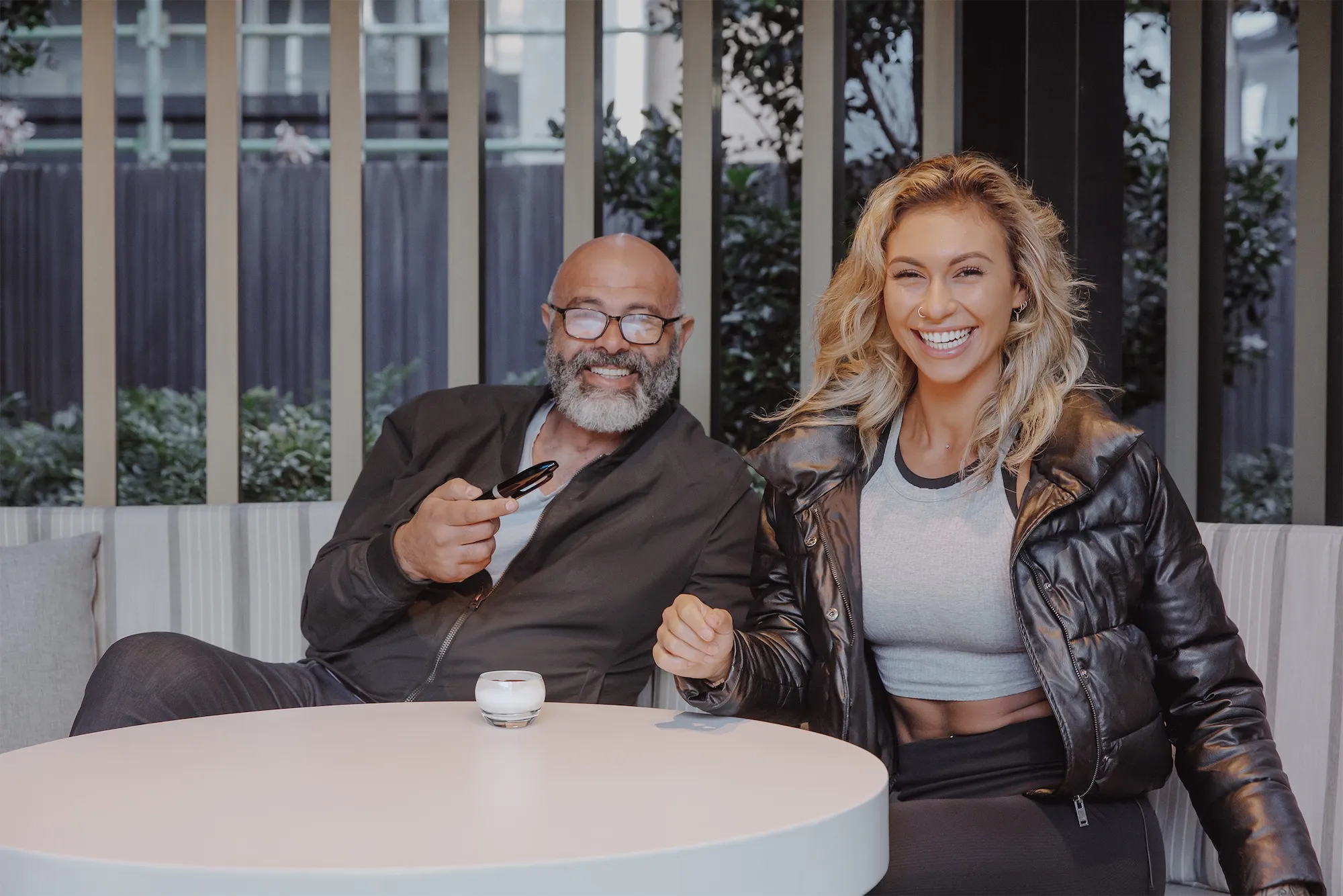 A man and a woman laughing together sitting at a table, one is holding a pen and they are enjoying a relaxed, happy moment.