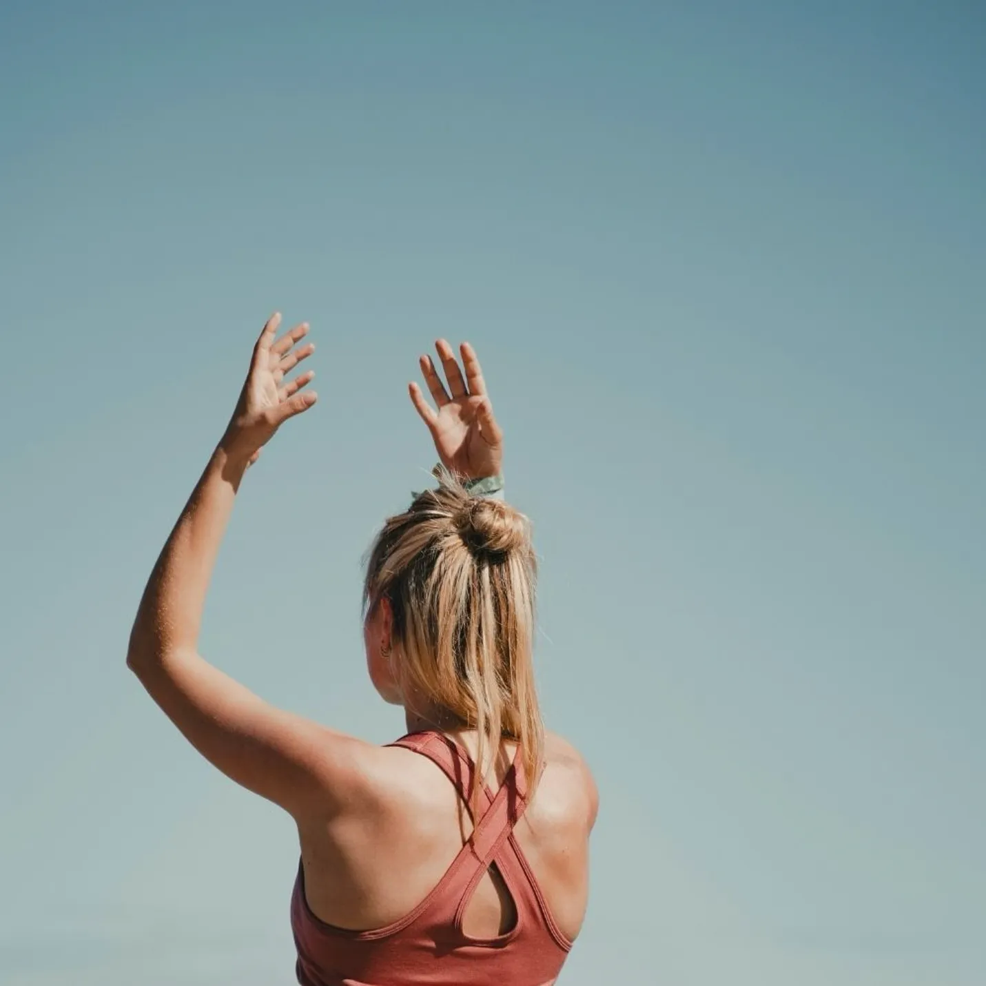 A woman facing away from the camera in a yoga pose on a clear day outdoors.