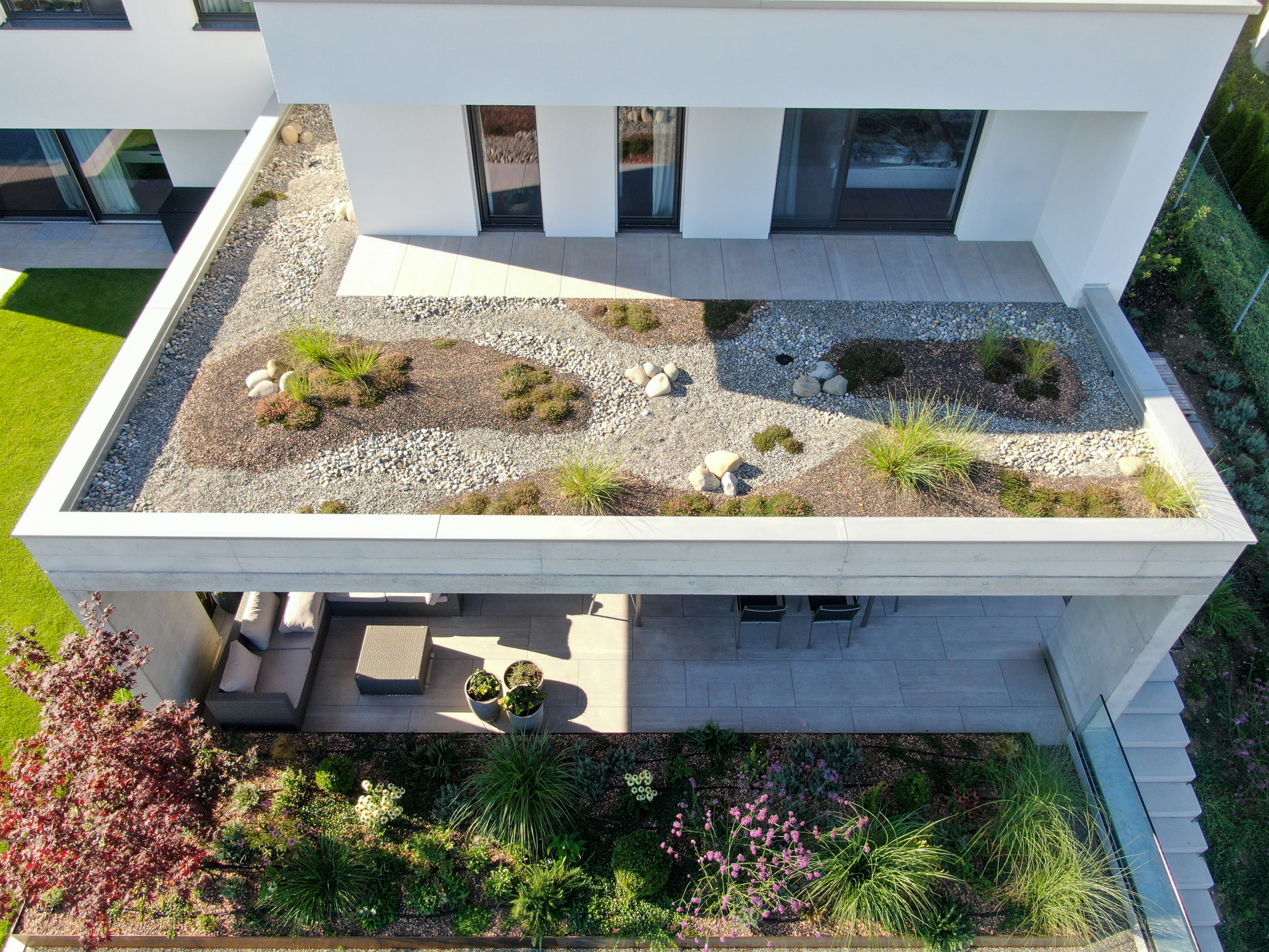 Villa mit Dachbegrünung, Bodendecker Pflanzen, im EG Sitzplatz mit üppigem Pflanzenbeet. 