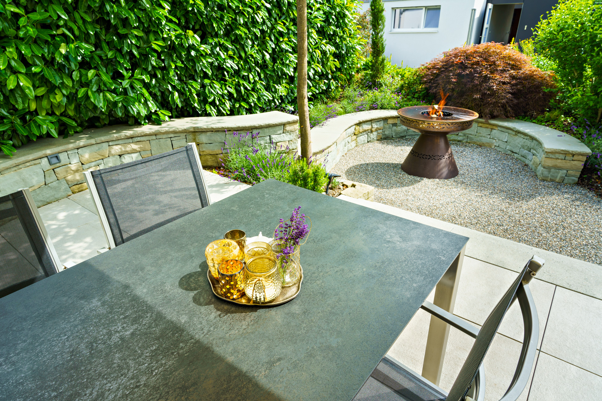 Sitzplatz mit Trockensteinmauer und Feuerschale und natürlich grüner Umgebung. 