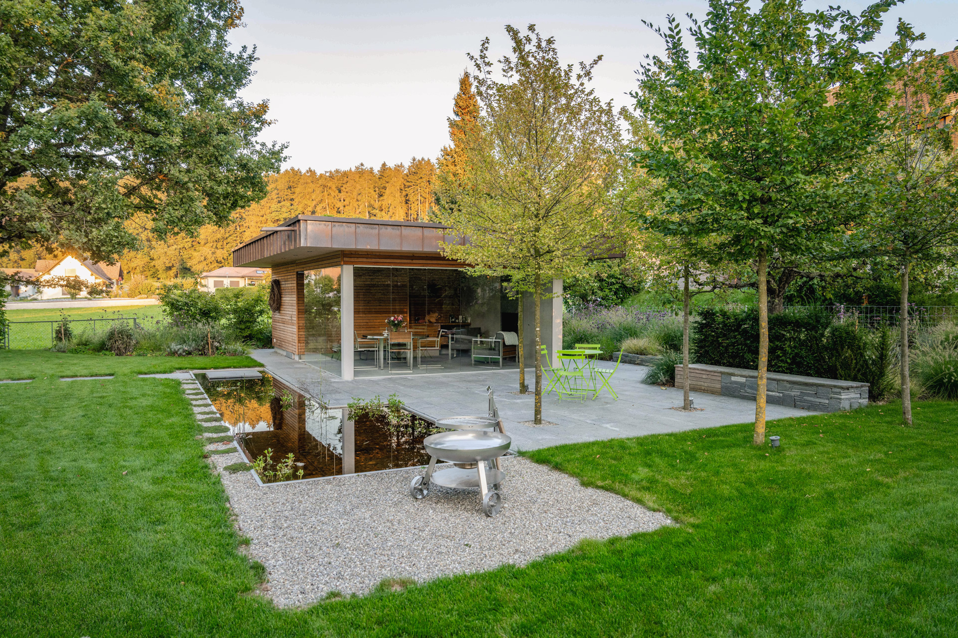 Loggia in einem grossen Garte mit Rasen, Kiesplatz, Sitzplatz aus Natursteinplatten und einem Wasserbecken. 