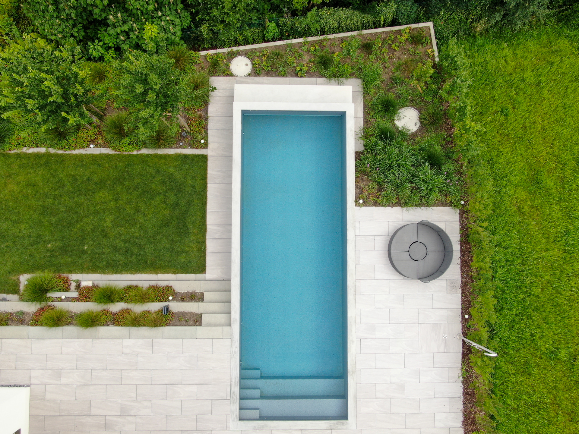 Infinity-Pool mit Natursteinsitzplatz in grünem Garten aus der Vogelperspektive. 
