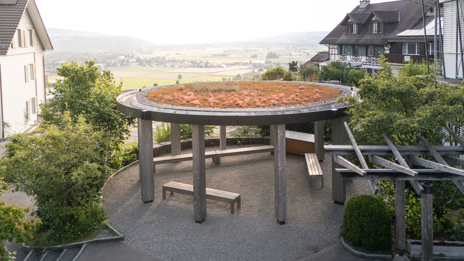 Runder, rot begrünter Pavillon mit einem Haus Links eines Rechts und Weitsicht in der Mitte. 