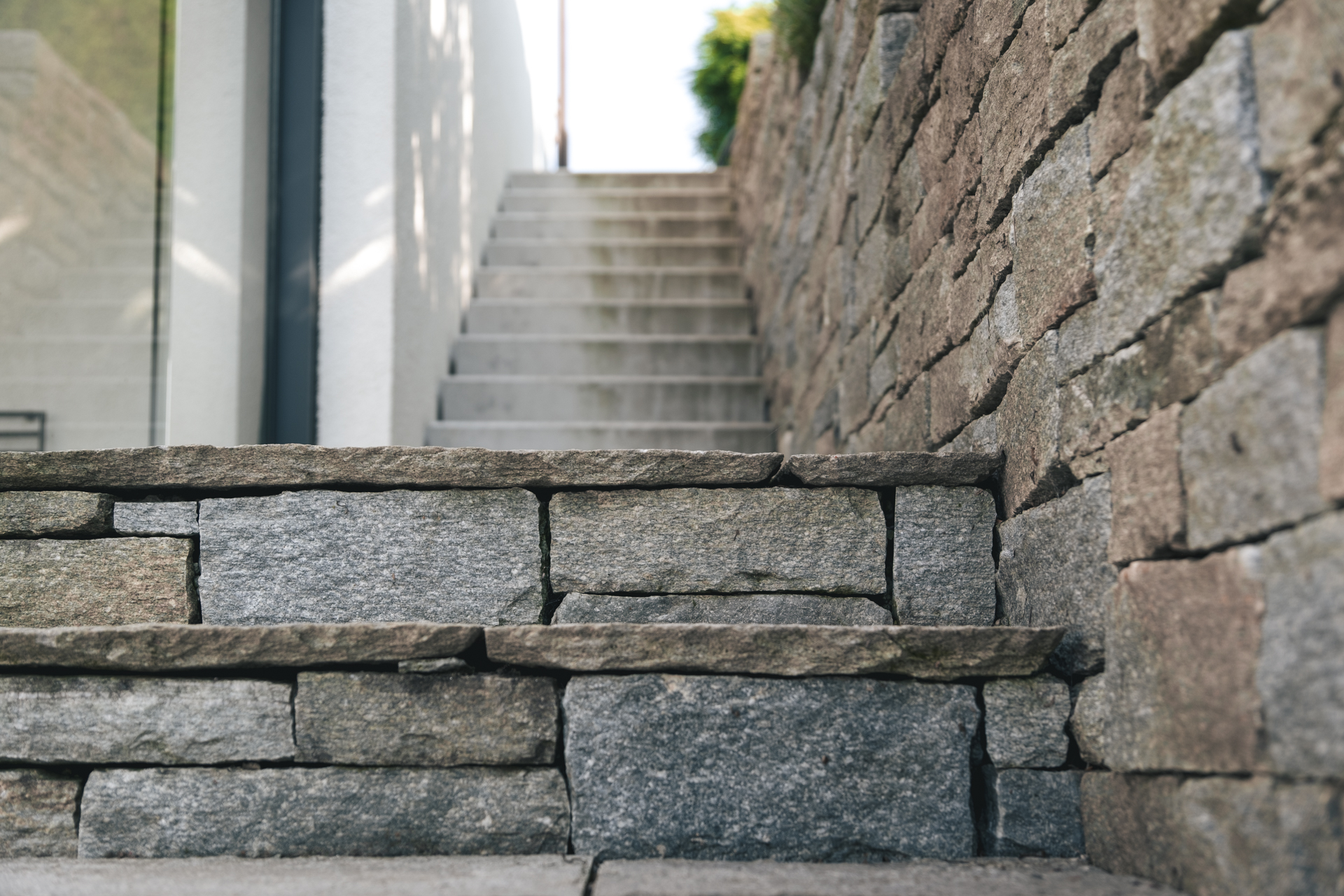 Natursteintreppe und Mauer neben Privathaus. 