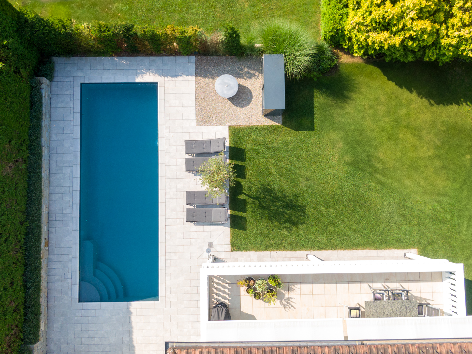 Grosser Rasen und Steinterrasse mit vier Sonnenliegen und Swimmingpool. 