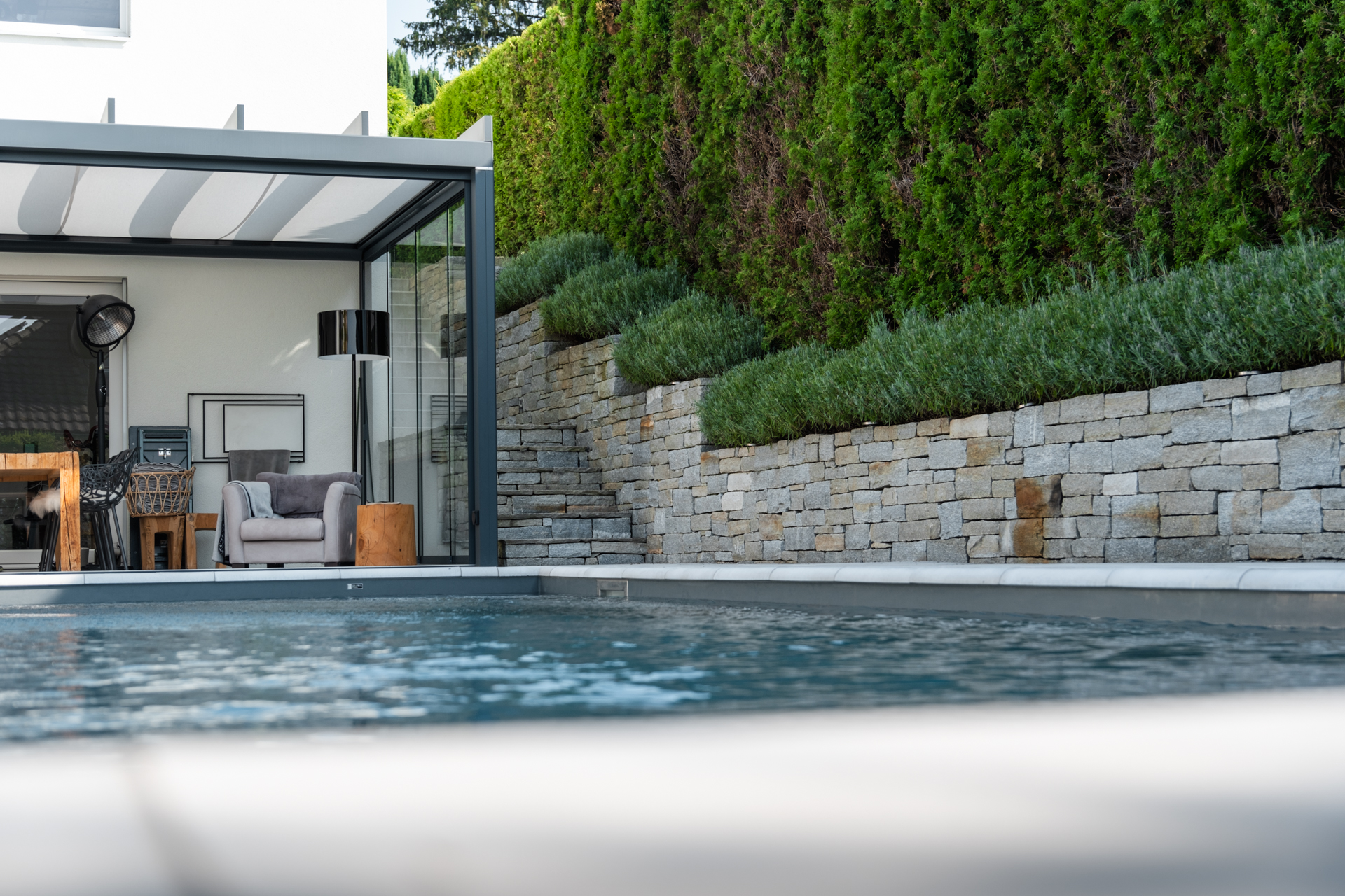 Bild im Vordergrund Swimmingpool, im Hintergrund Natursteinmauer mit Lavendel und Sichtschutzhecke. 