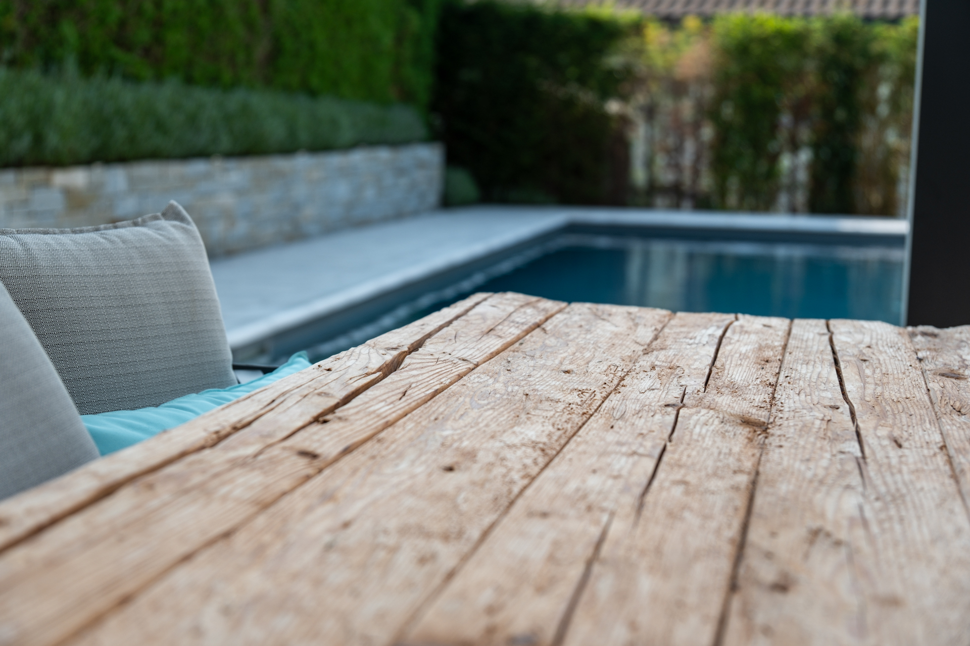 Altholztisch im Detail mit Swimmingpool unscharf im Hintergrund. 
