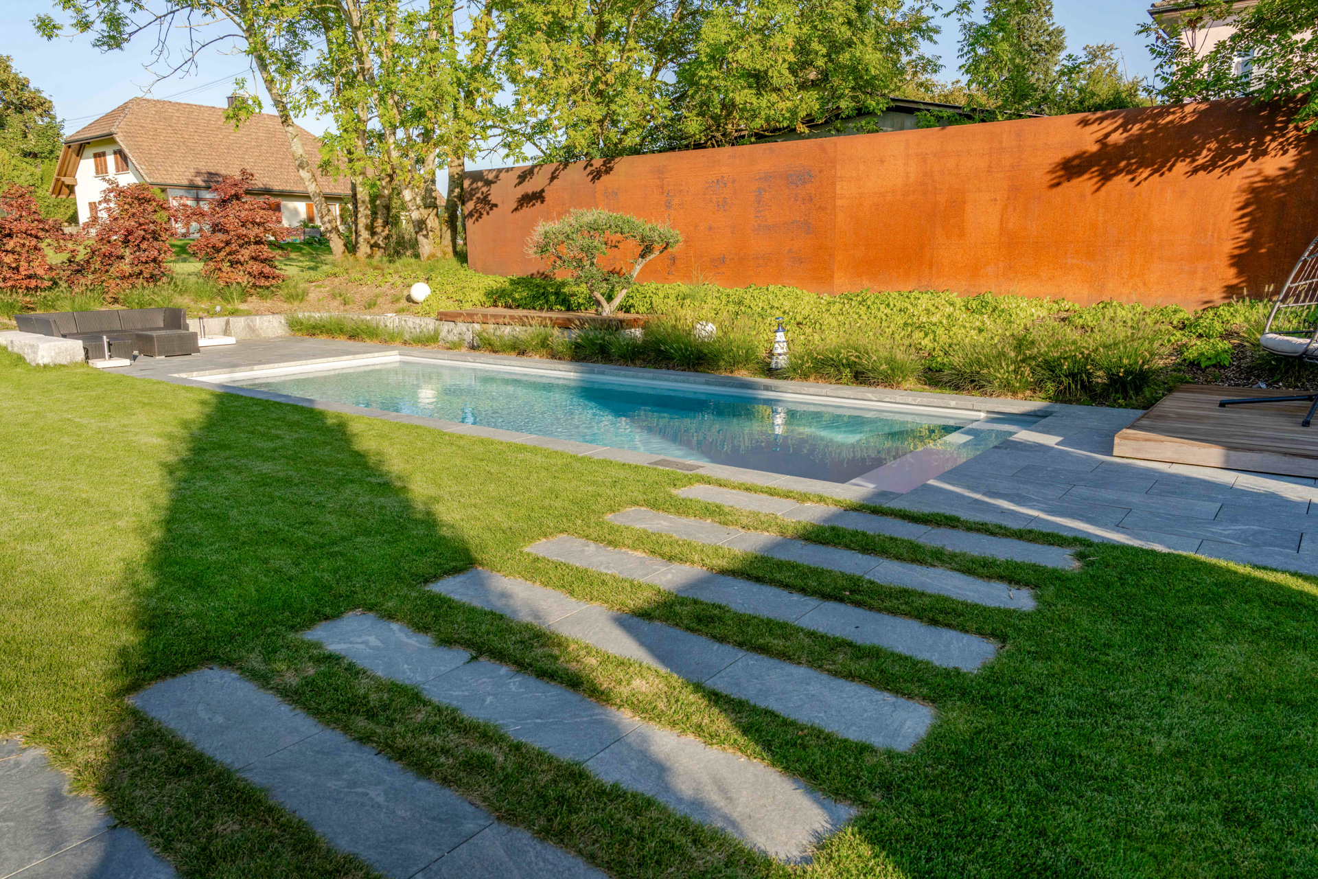 Garten mit Swimmingpool und hoher rostroter Stahl Sichtschutzwand. 