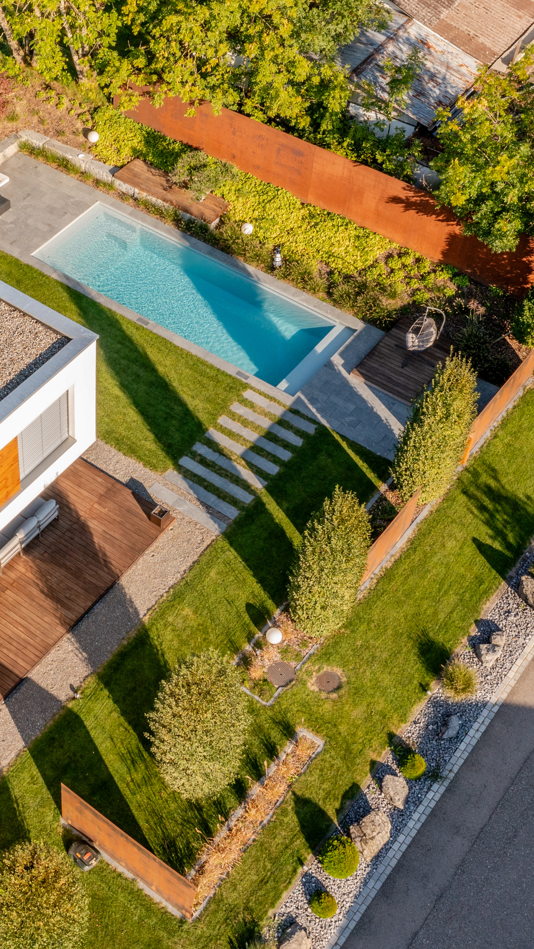 Vogelansicht eines Garten mit grossem Swimmingpool hohen rostroten Sichtschutzwänden und schönen Bäumen. 