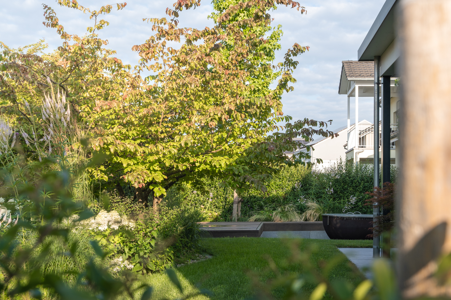 Garten mit einem Feuerring und einer Holzsitzbank inmitten von wunderschönen Bäumen. 