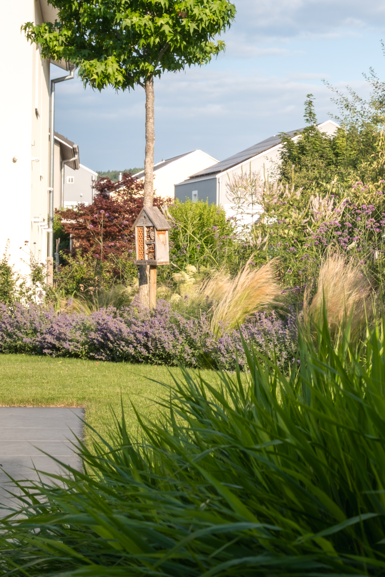 Garten mit saftiger Wiese, Naturstein Terrasse und farbigen Stauden. 