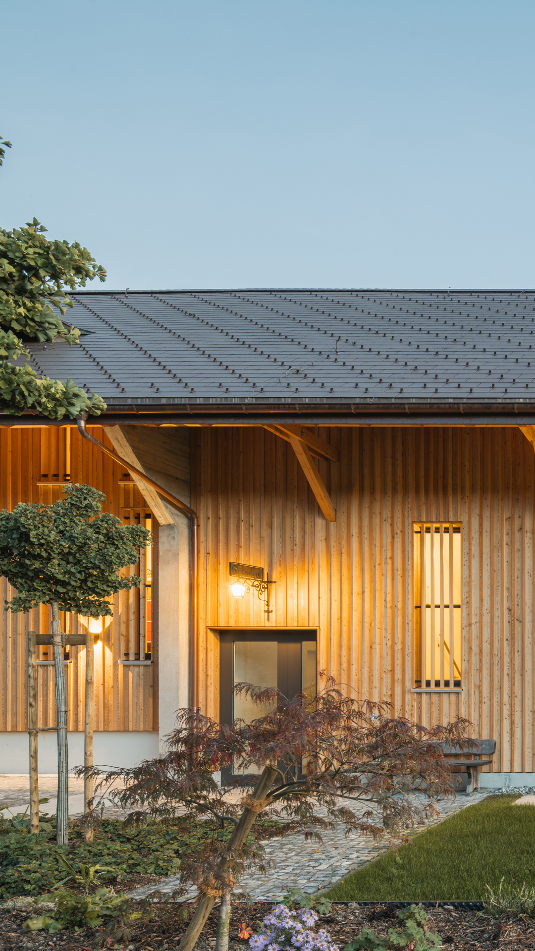 Holzverkleidetes Haus mit Outdoorbeleutung und schöne Begrünung. 