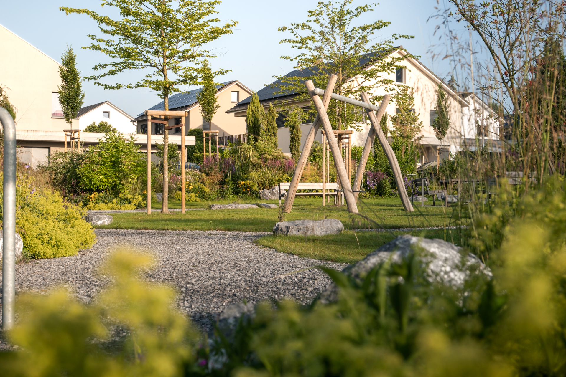 Spielplatz mit grünen Stauden im Vordergrund und hochstämmigen Bäumen.