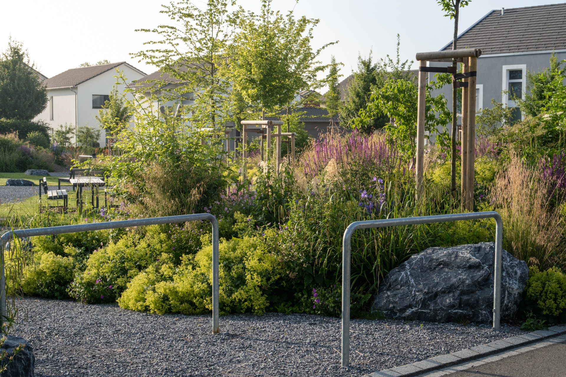 Kiesweg mit Speedblocker, im Hintergrund blühende Stauden und Blumenbeete.