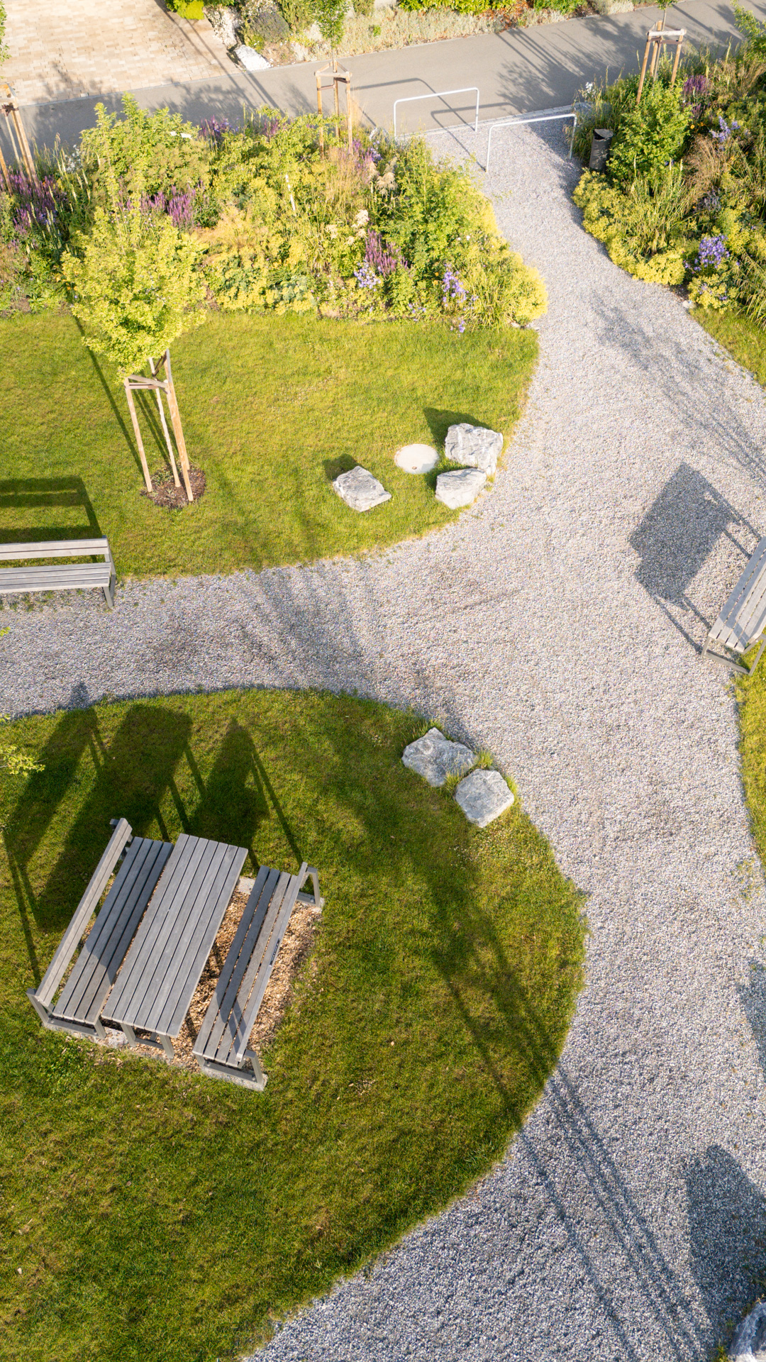 Drohenaufnahme eines Stadtparkes mit Sitzbank und geschwungenen Kieswegen.