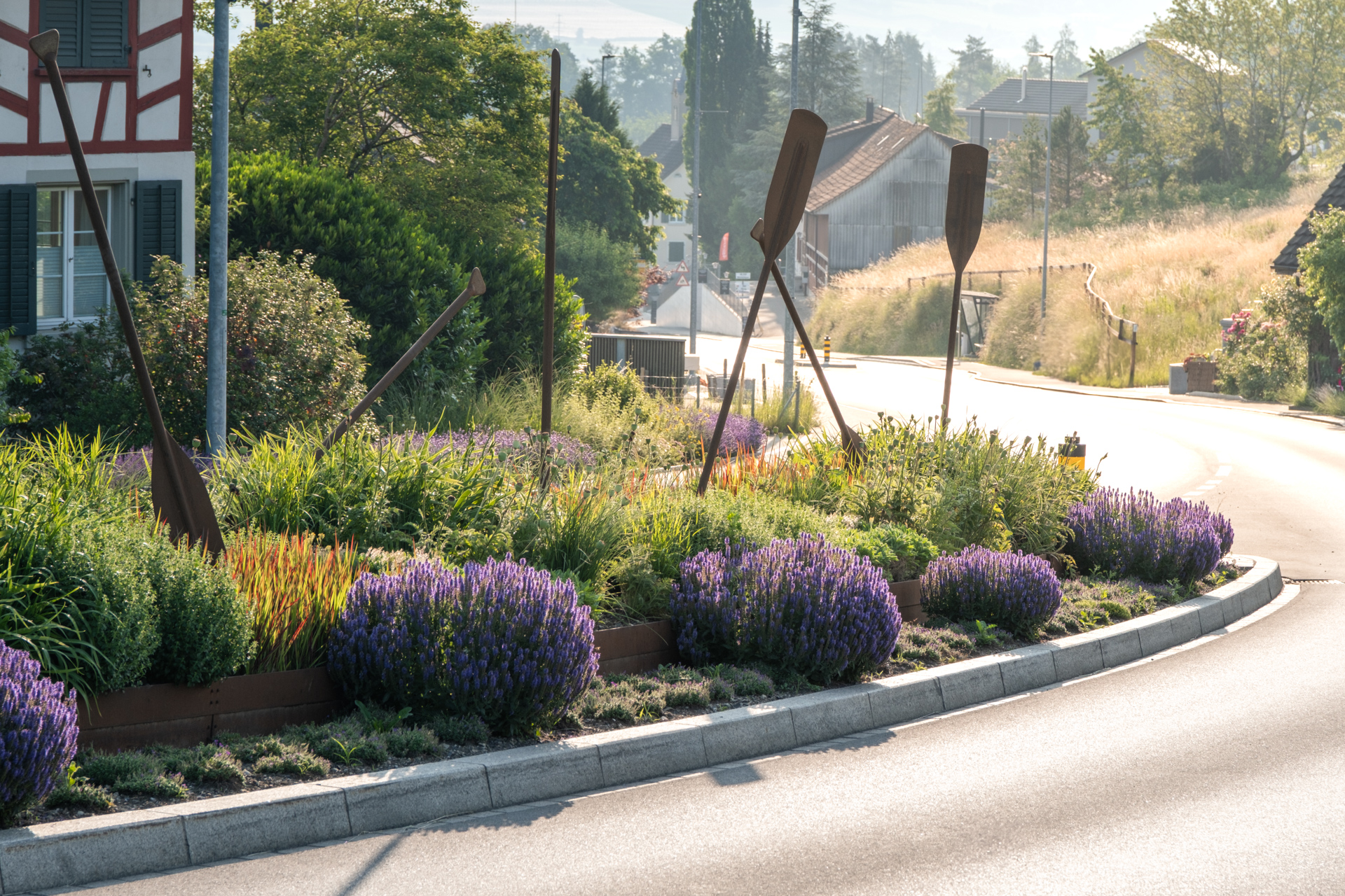 Strasse in gleissendem Sonnenlicht und violett blühendem Lavendel auf der Verkehrsinsel.