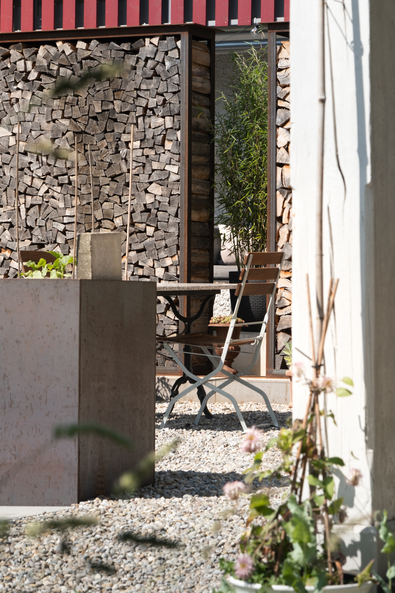 Stahlhochbeet im HIntergrund ein Gartenstuhl und eine Holzscheiterbeige mit Stahlrahmen.