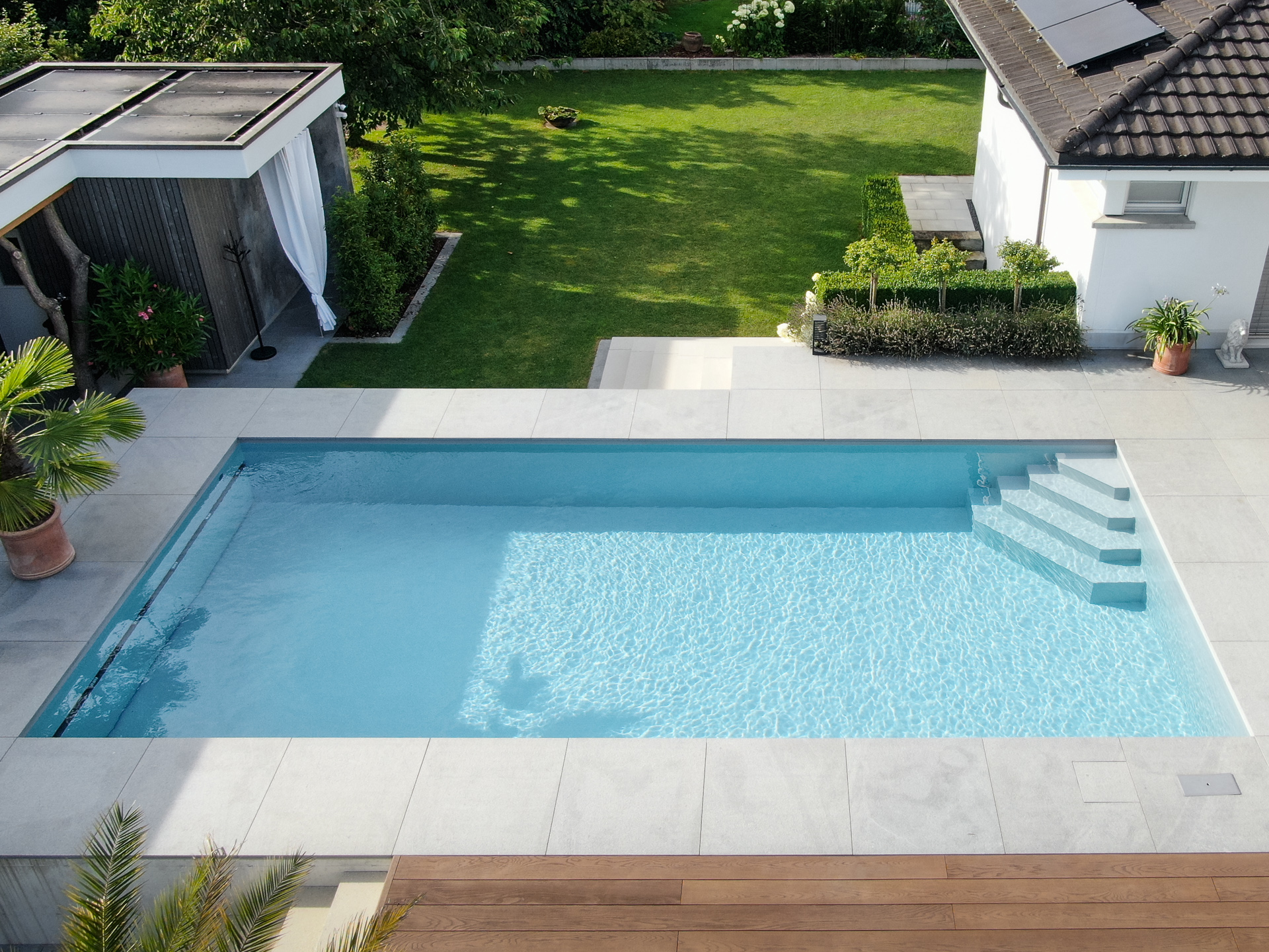 Grosser Swimmingpool mit Holzrost und grosser Rasenfläche. 