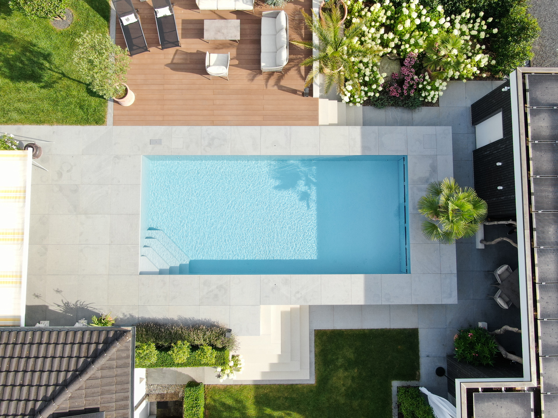 Swimmingpool in der Vogelansicht mit Holzterrasse und Spielwiese. 