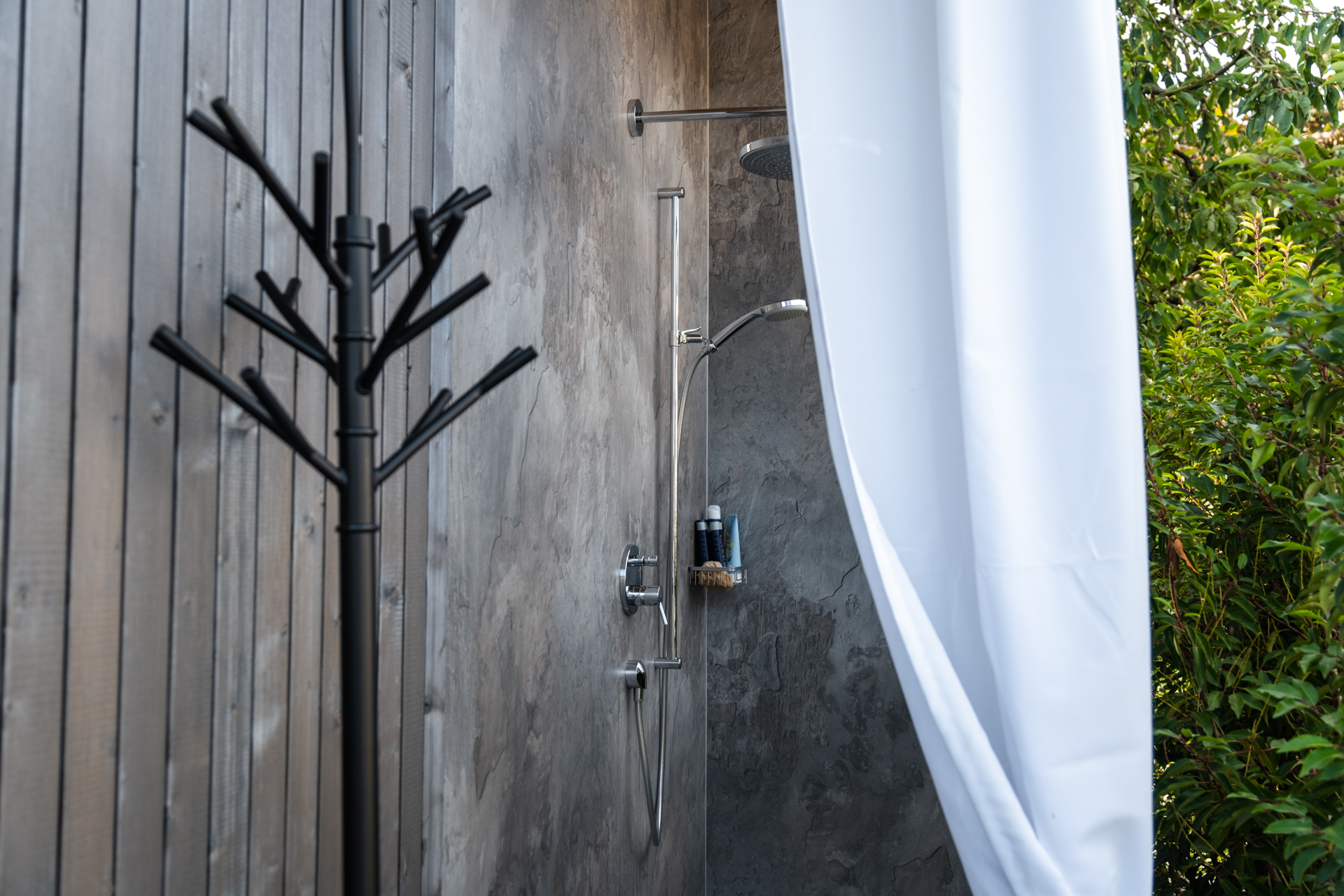 Outdoordusche mit weissem Vorhang und viel Grün im Hintergrund. 